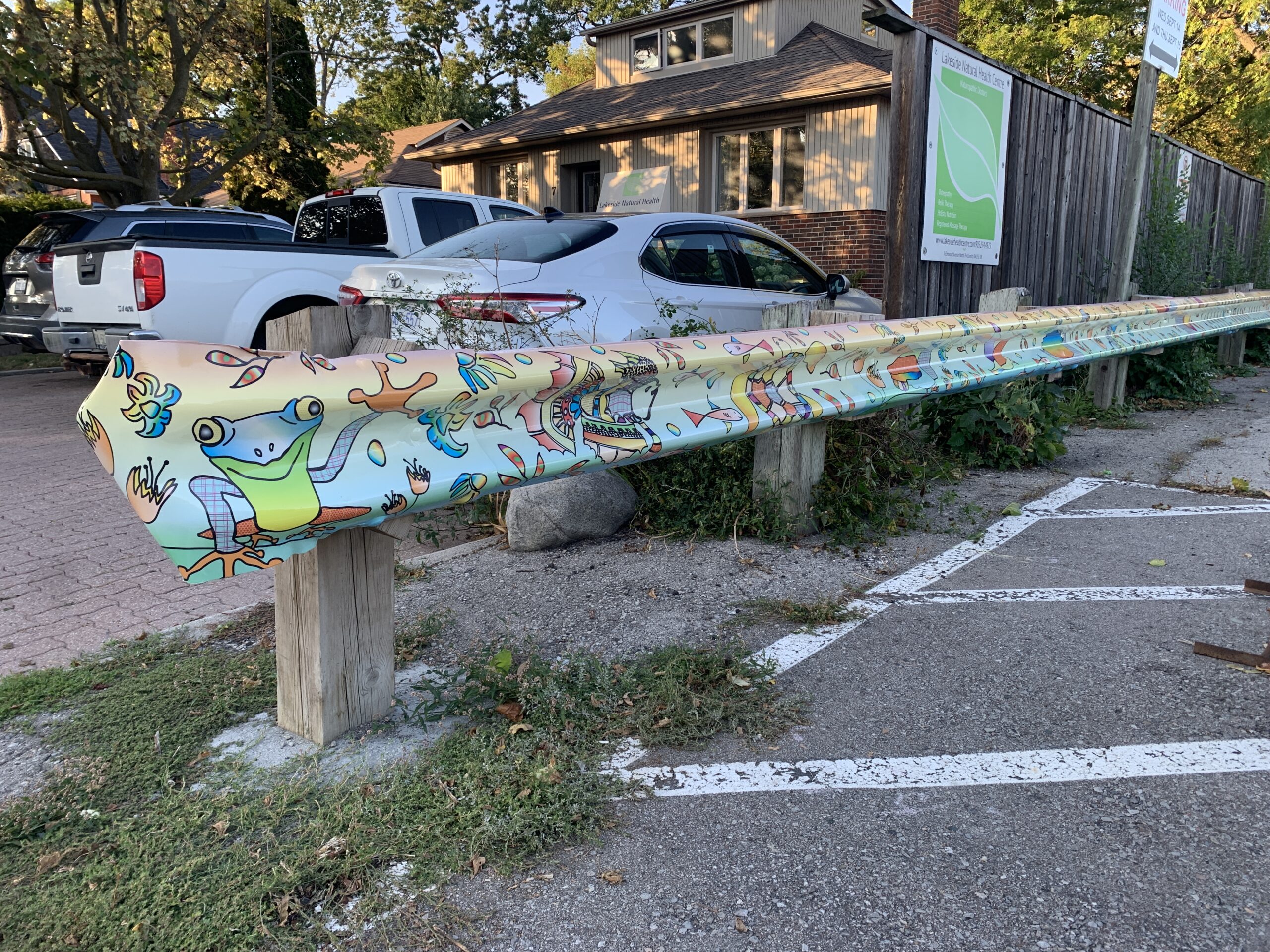 A digital mural on a guardrail in a parking lot. The illustration is of fish, animals, and flowers in a rainbow of pastel tones, against a gradient pastel rainbow backdrop.