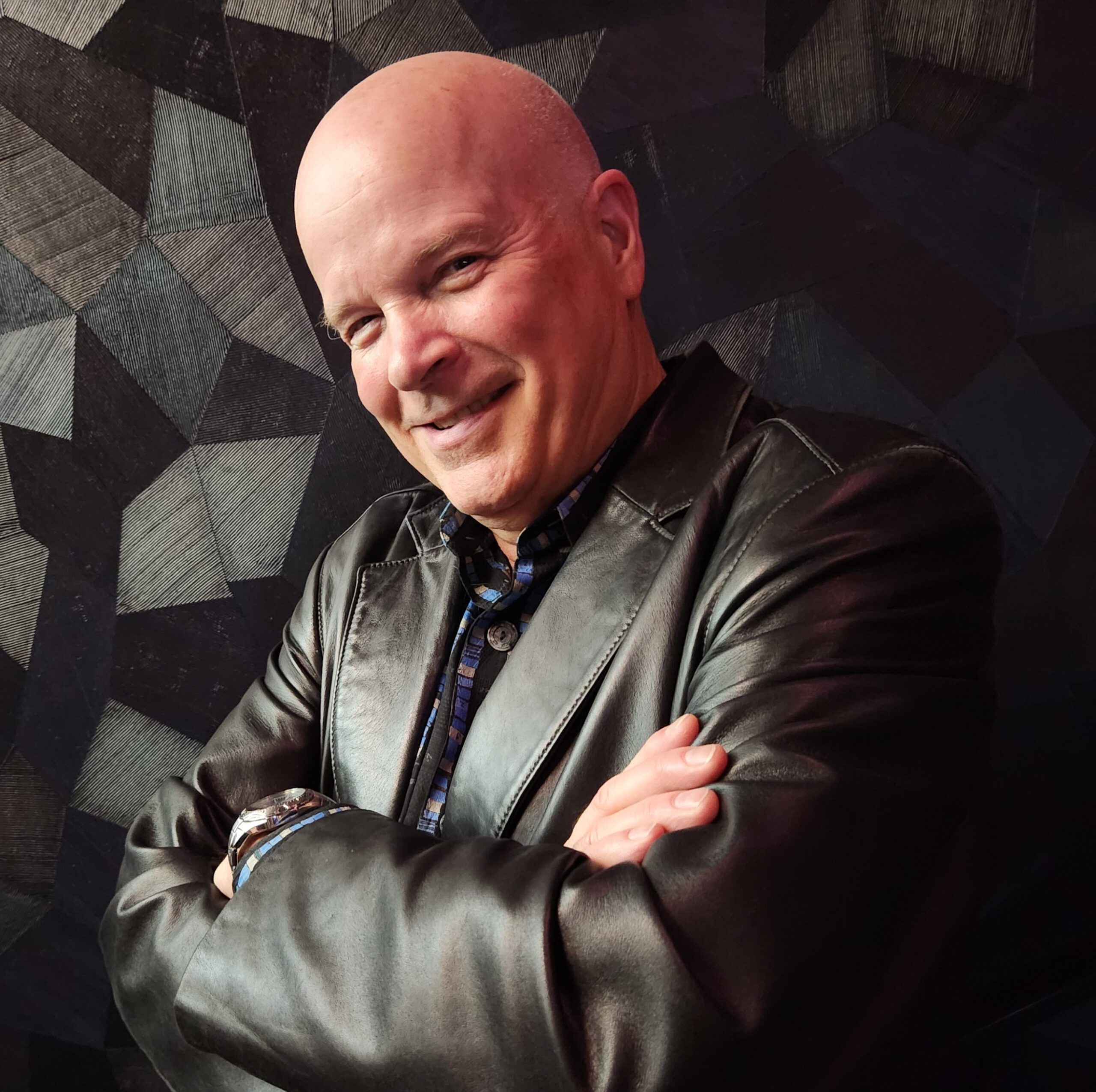 Mike Douglas, Executive Director, smiling in front of a black fabric background wearing a leather jacket