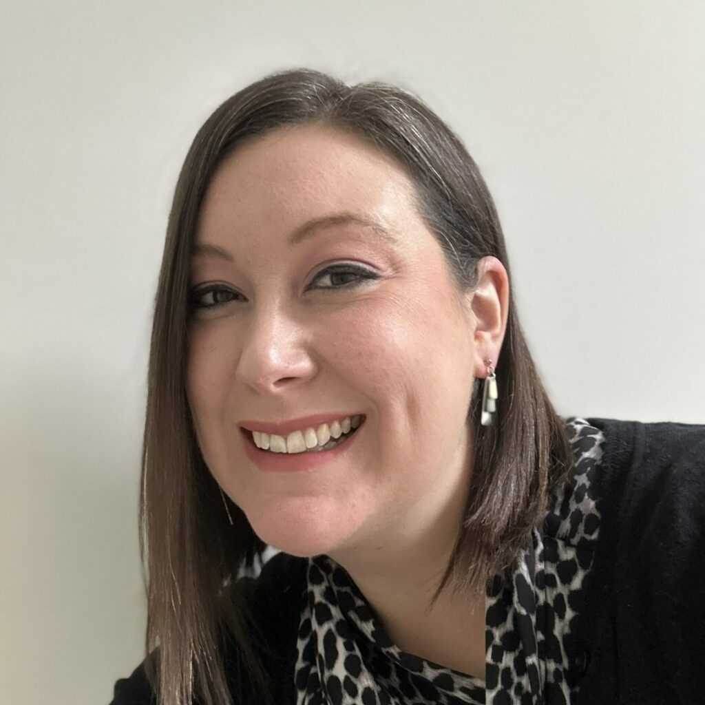 Susan Durnin, Operations & Development Manager, smiles wearing a blouse and cardigan in front of a beige wall.