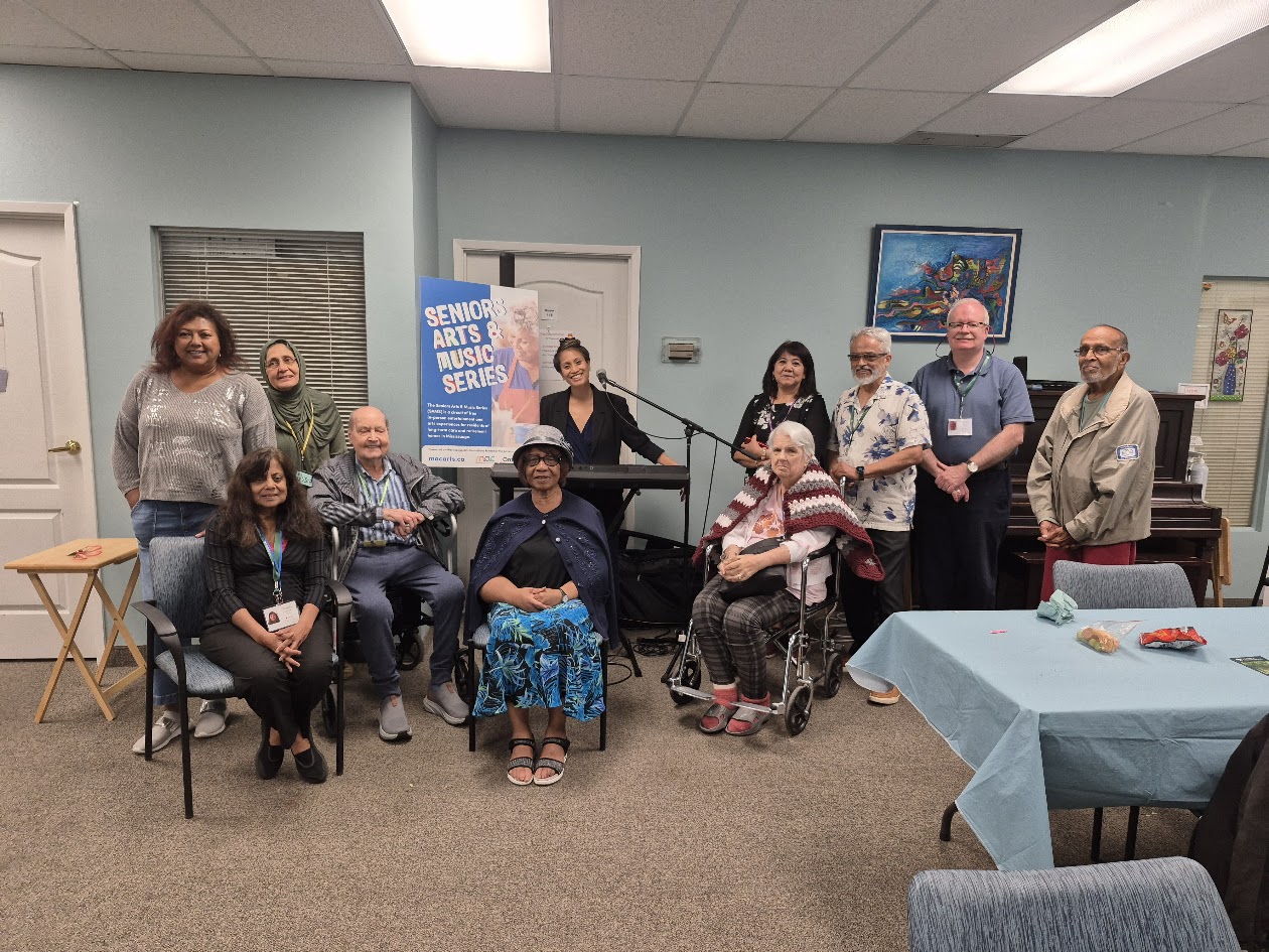 A woman (Arlene) smiling and interacting with a senior resident in a brightly lit hospice common room.
