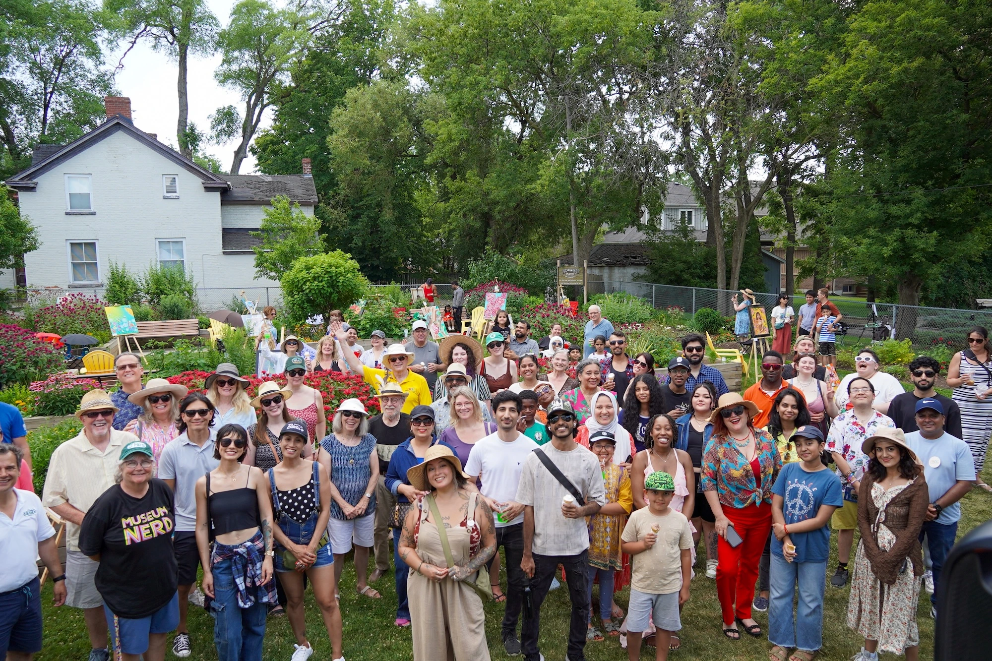 A large group of diverse people posing for a photo on a lawn during a community art festival in a garden.