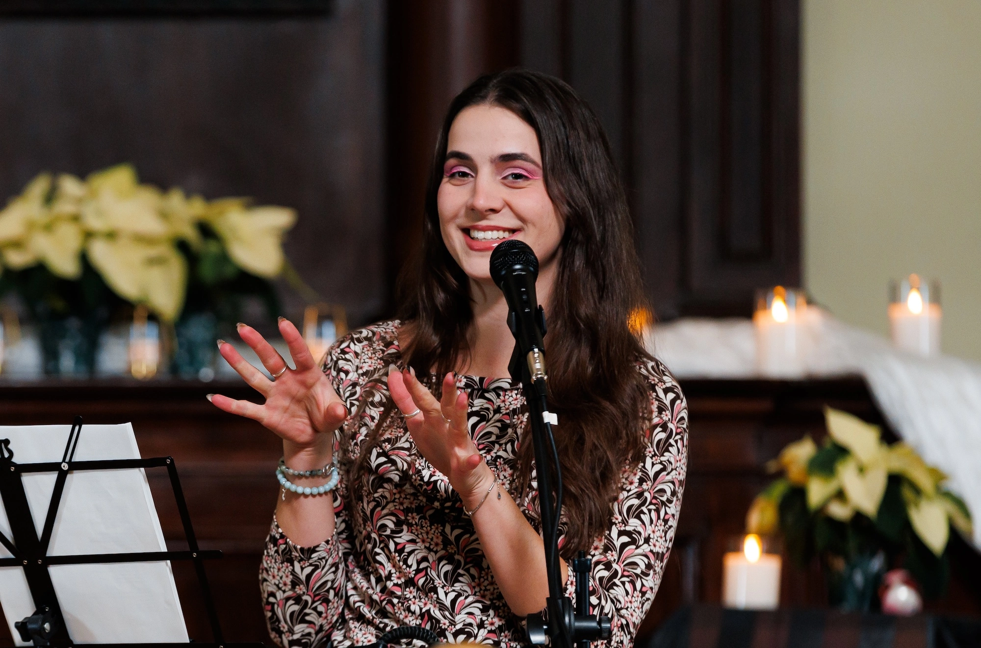 Headshot of Andrea Josic, who smiles and speaks enthusiastically with her hands in motion in front of a microphone.