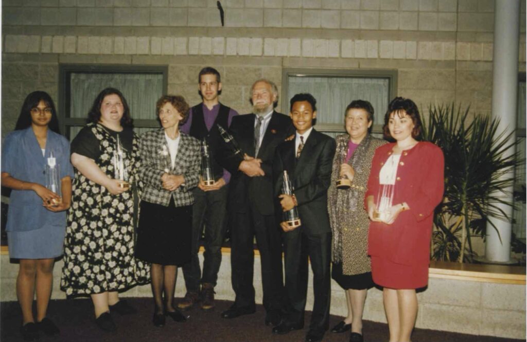 Eight winners of the 1994 Mississauga Arts Awards stand in the lobby of Meadowvale Theatre, holding their awards.
