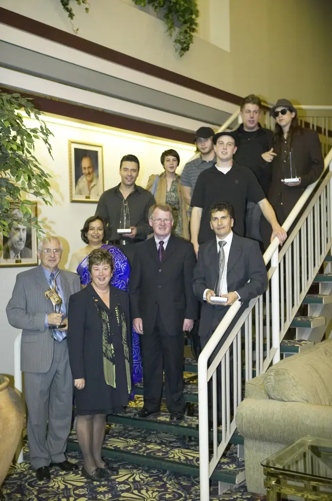 Winners of the 2007 Mississauga Arts Awards post on a staircase at Stage West, holding their geometric glass trophies. 