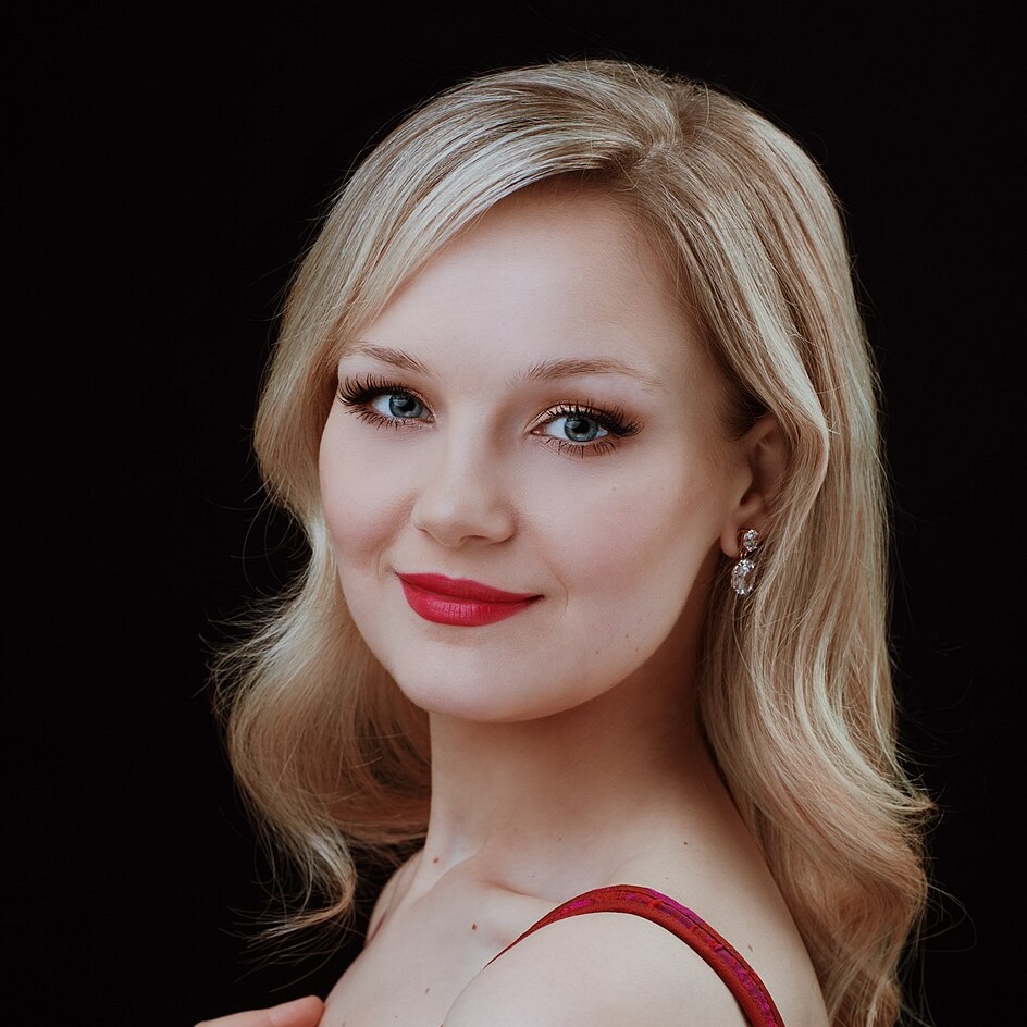 Headshot of Karoline Podolak, smiling against a black backdrop, wearing a red tank dress.