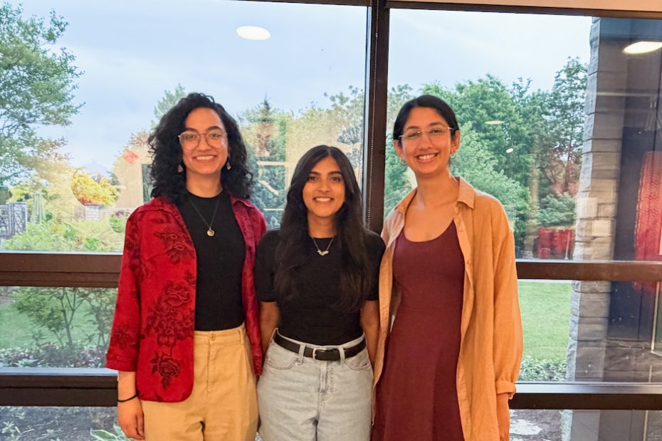 Three smiling people standing side-by-side posing for a photo in front of a large window.