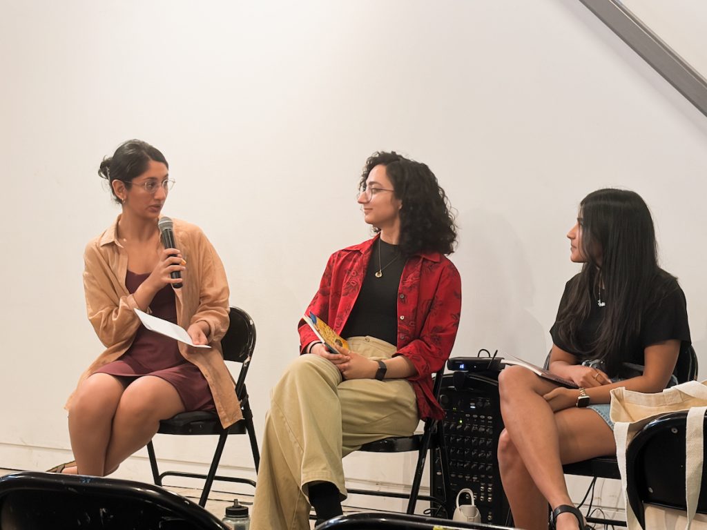Three people sitting in chairs on stage during a panel discussion, with one woman speaking into a microphone.