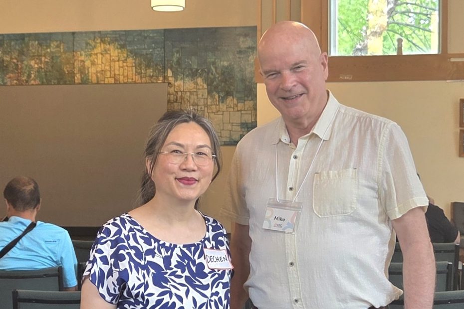 A woman in a blue patterned top and a man in a button-down shirt posing together behind a book display table.