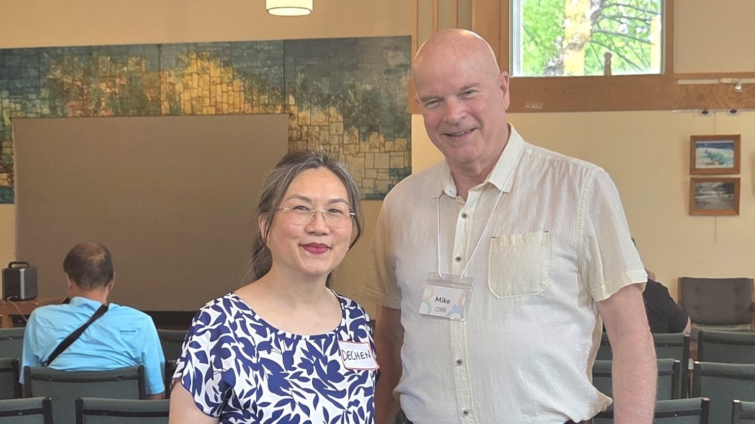 A woman in a blue patterned top and a man in a button-down shirt posing together behind a book display table.