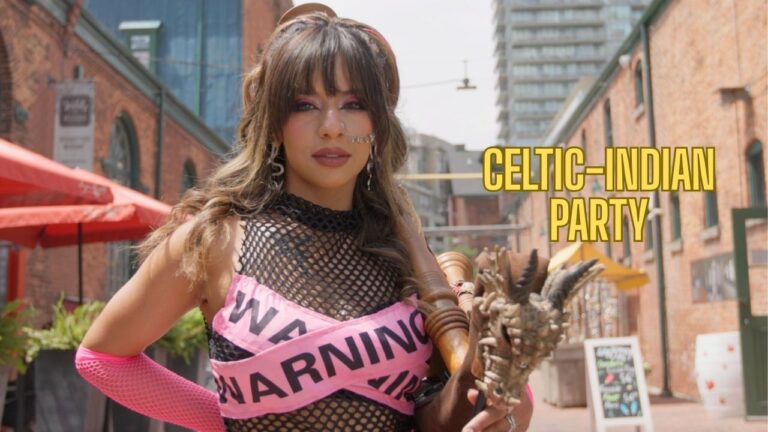 A woman with long wavy hair and bold makeup poses outdoors on a brick street. She wears a black fishnet top crossed with pink "WARNING" tape, holds the chanter of a bagpipe decorated with a small dragon head, and yellow text to the right reads "CELTIC-INDIAN PARTY."
