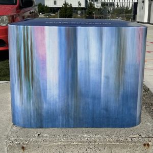 Utility box covered in an abstract mural in blurred vertical lines of pastel blues, pinks, and grey. The mural is by Sherry Prenevost.