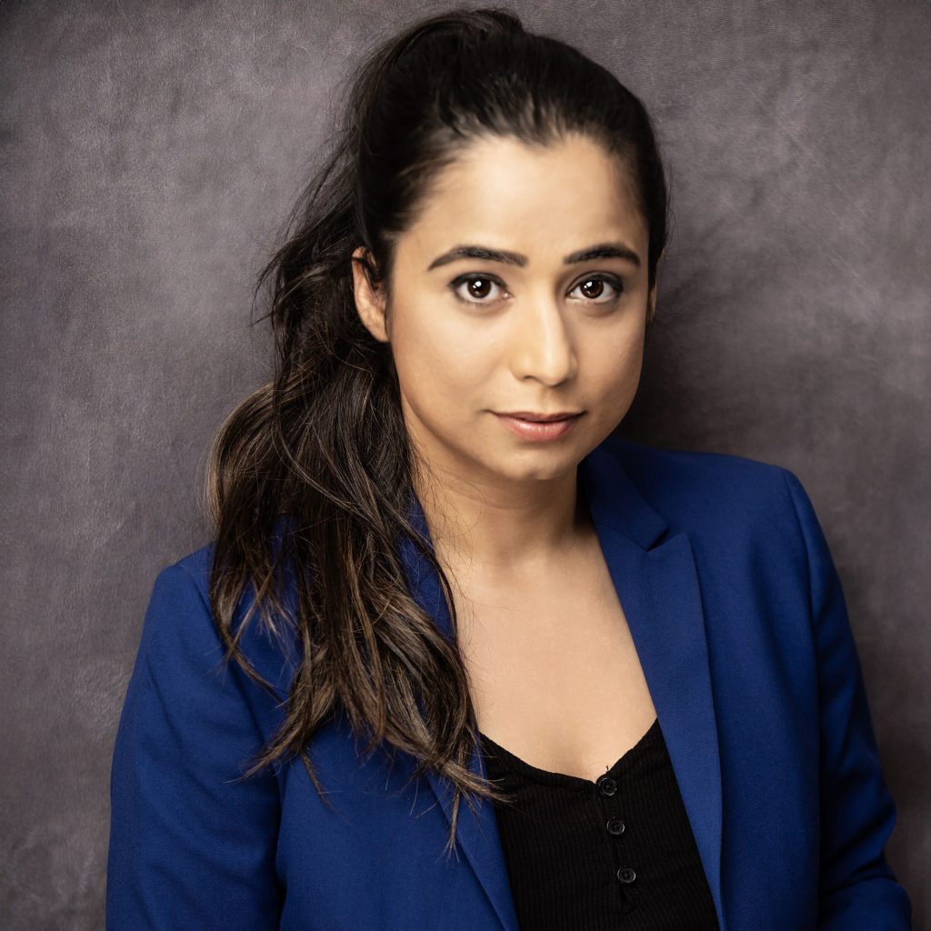 Megha Raina, Community Partnerships & Events Coordinator, looks into camera wearing a blue blazer in front of a grey wall.